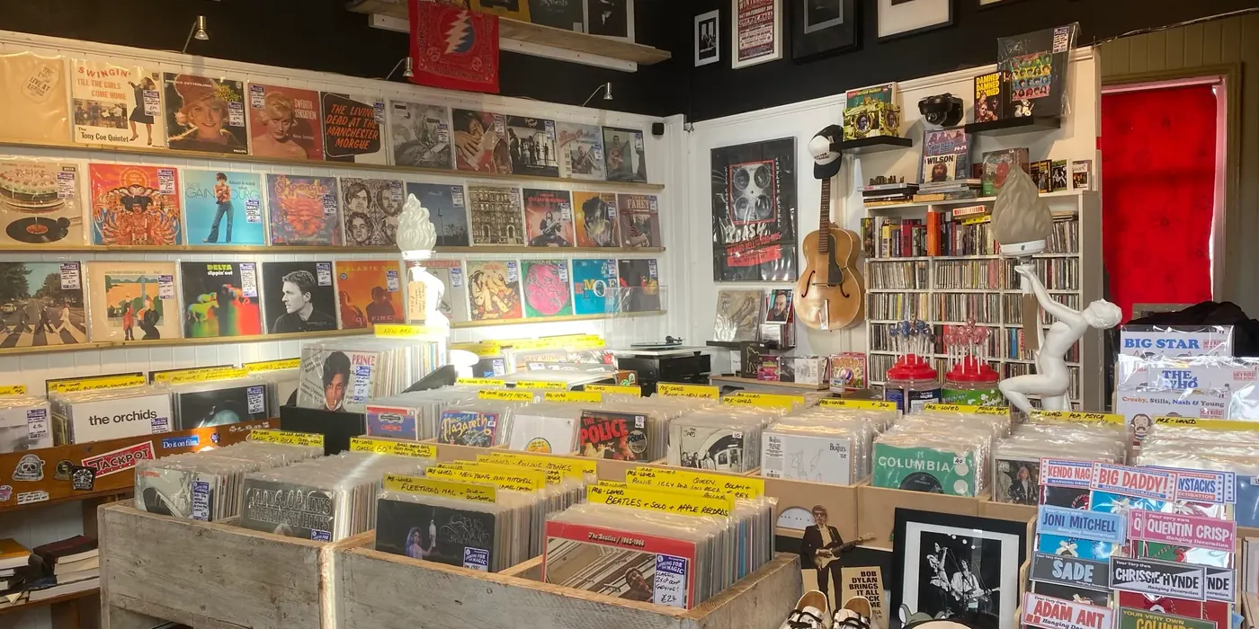 Inside the shop: racks of records down the middle, sleeves and framed prints covering the wall, and a guitar hanging up.